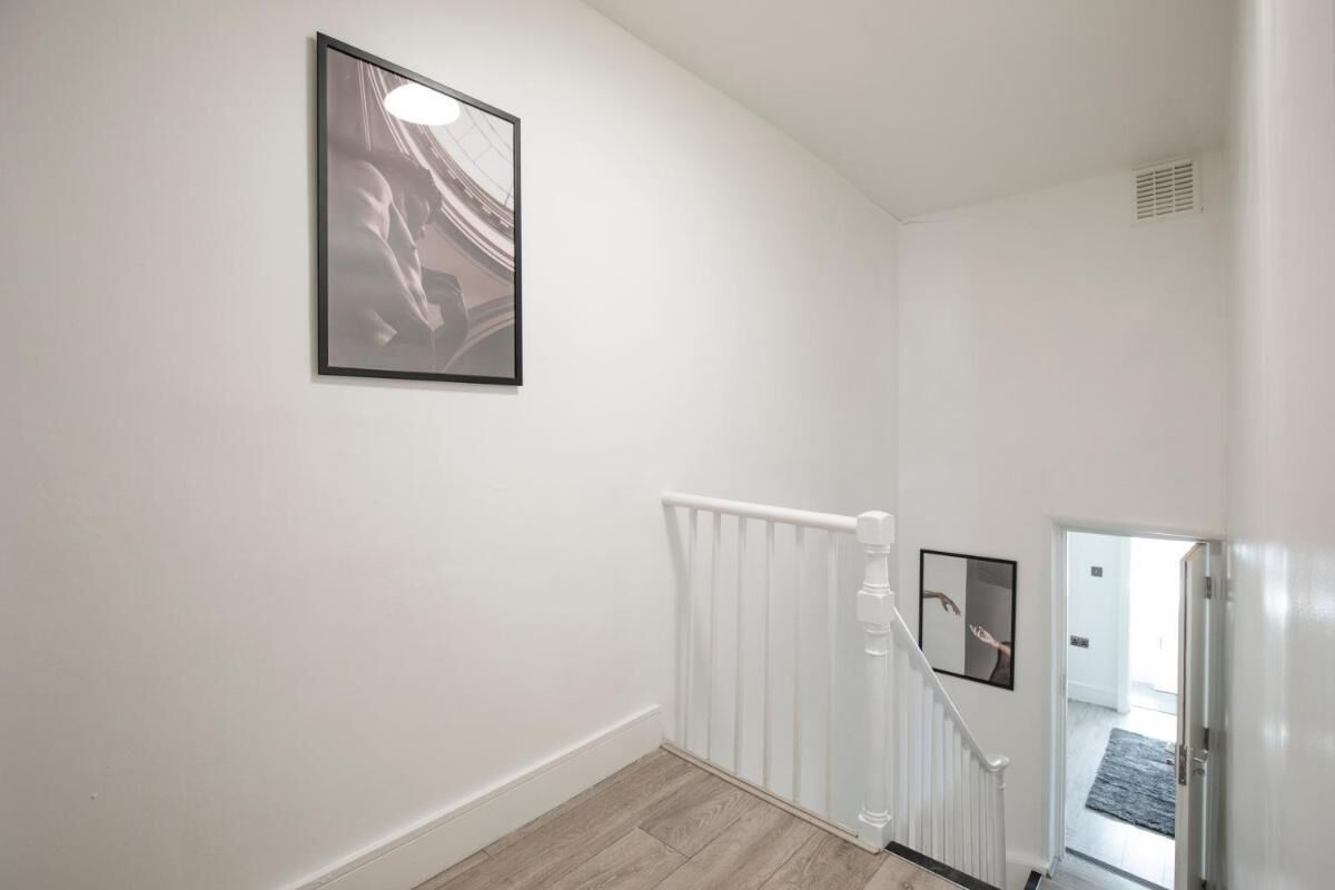 A clean, white-walled hallway with a wooden floor, a white radiator, and a staircase with a handrail.