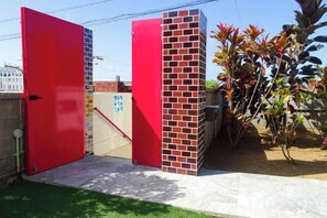 A gated entrance with a red door and a brick wall, a wheelchair-accessible ramp, and a small garden area with plants. - Minshuku Itoman Bettei Goyukkuri (Itoman)