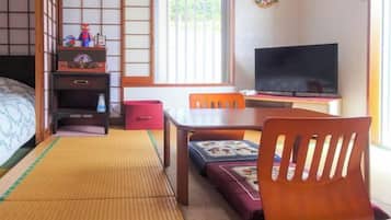 Une pièce de style japonais traditionnel, avec un sol recouvert de tatamis, un futon servant de lit, une télévision, une table en bois et un fauteuil futon.