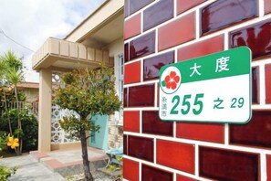 Una placa con una dirección residencial en una pared de ladrillo, con un pequeño árbol en primer plano.