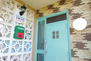 Una puerta color turquesa con cerradura de seguridad, una máquina de pago verde y una pared decorativa con diseño geométrico.
