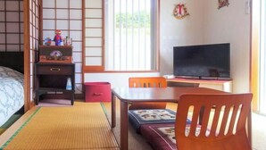 Een traditionele Japanse kamer met tatami vloerbedekking, een lage tafel, een televisie en een futonbed.