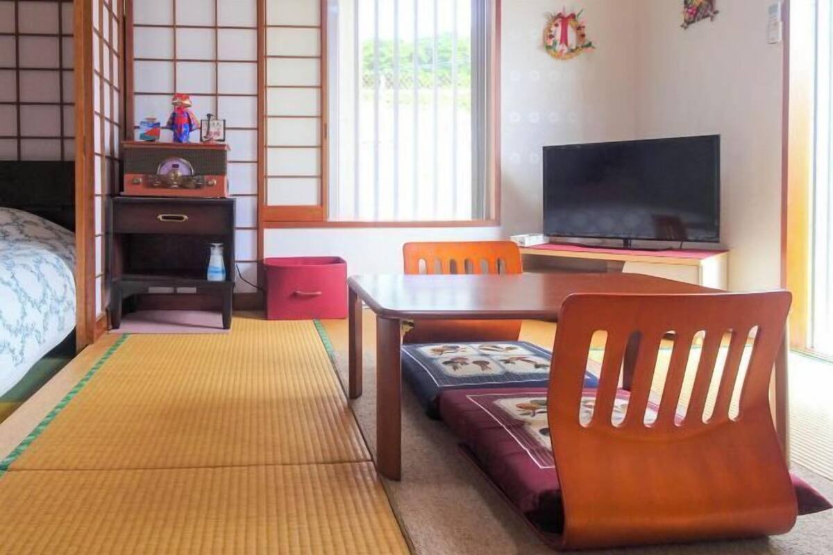 A traditional Japanese-style room with tatami flooring, a low table, a television, and a futon bed.