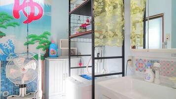 Una habitación con un armario blanco, una lavadora blanca, un ventilador y una estantería con diversos objetos.