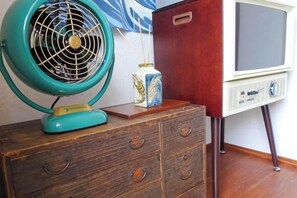A vintage television set on a wooden stand, a teal fan on a wooden dresser, and a decorative box. - Minshuku Itoman Bettei Goyukkuri (Itoman)