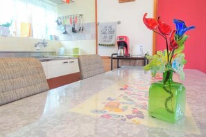 A dining table with a floral centerpiece, a kitchen area with utensils, and a red wall. - Minshuku Itoman Bettei Goyukkuri (Itoman)