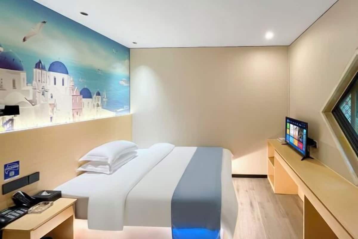 A hotel room with a bed, a desk with a phone, a TV, and a wall mural.