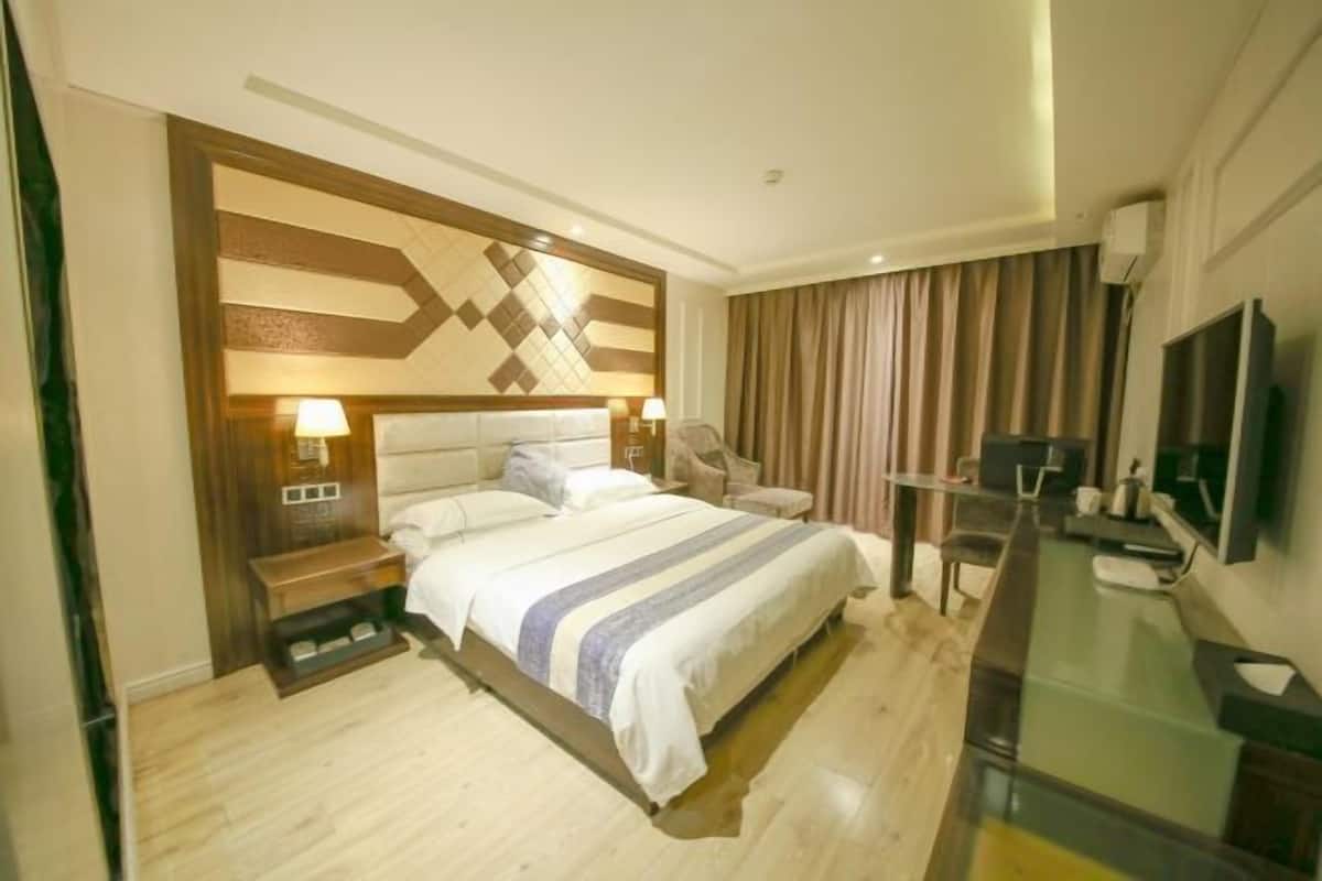 Habitació d'hotel amb llit, taules de nit, escriptori, cadira, televisió i una finestra gran amb cortines.