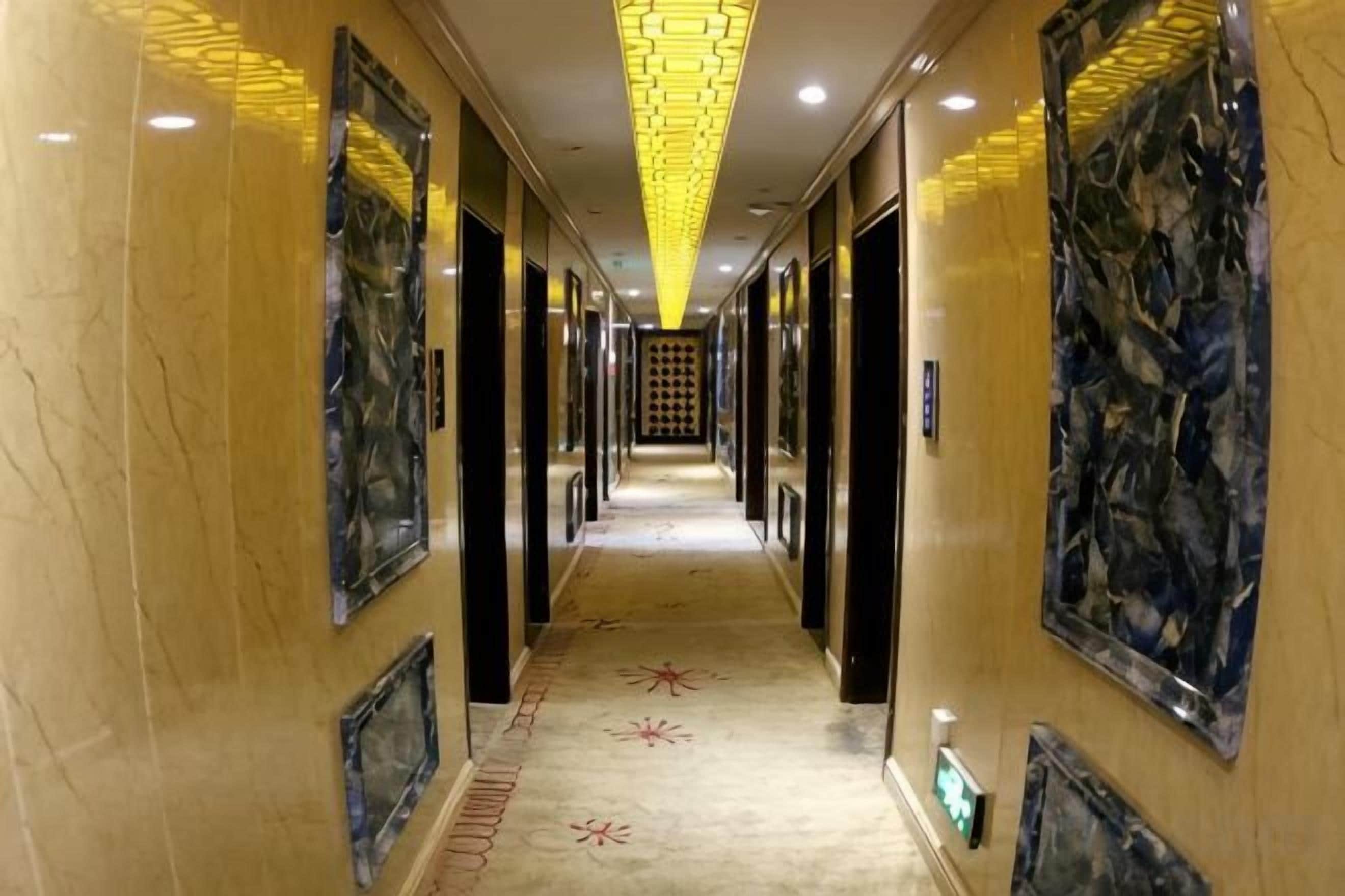 A hotel hallway with a marble floor, artwork on the walls, and a patterned carpet.