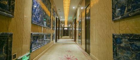 A hotel corridor with marble walls, framed artwork, and a carpet with a floral pattern.