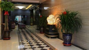 Un vestíbulo de hotel con piso a cuadros, plantas en macetas y un lámpara decorativa.