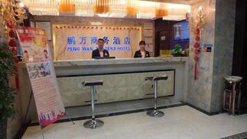 A hotel reception desk with a sign, two bar stools, and a decorative wall.