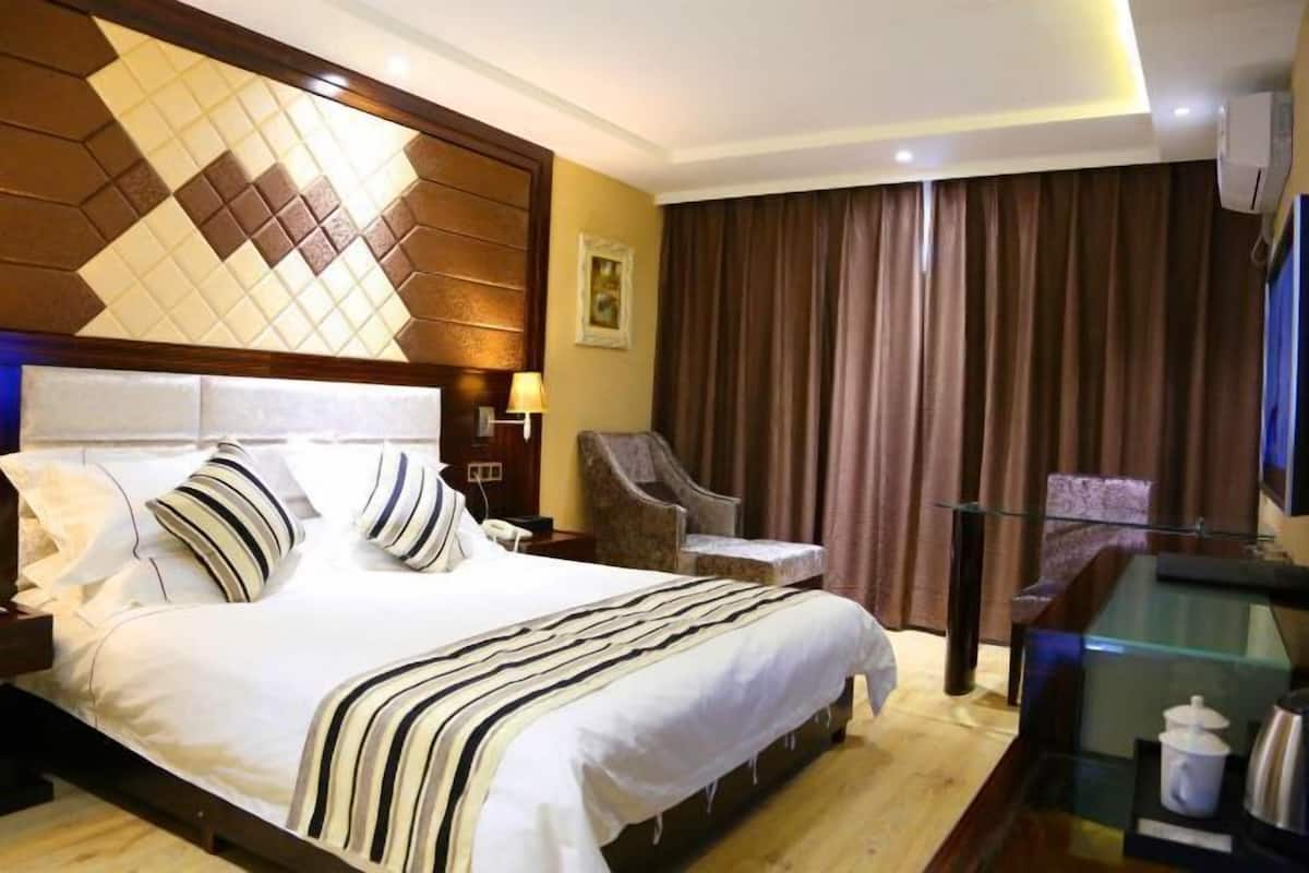 Una habitació d'hotel amb un llit gran, una cadira, un escriptori amb un separador de vidre i una finestra gran amb cortines.