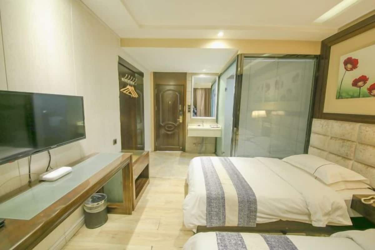 Habitació d'hotel amb llit, televisió, escriptori, mirall i bany visible a través d'una porta de vidre.
