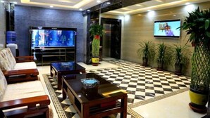 Un vestíbulo con suelo a cuadros, televisor de pantalla plana, sofás, una mesa de centro y plantas en macetas.