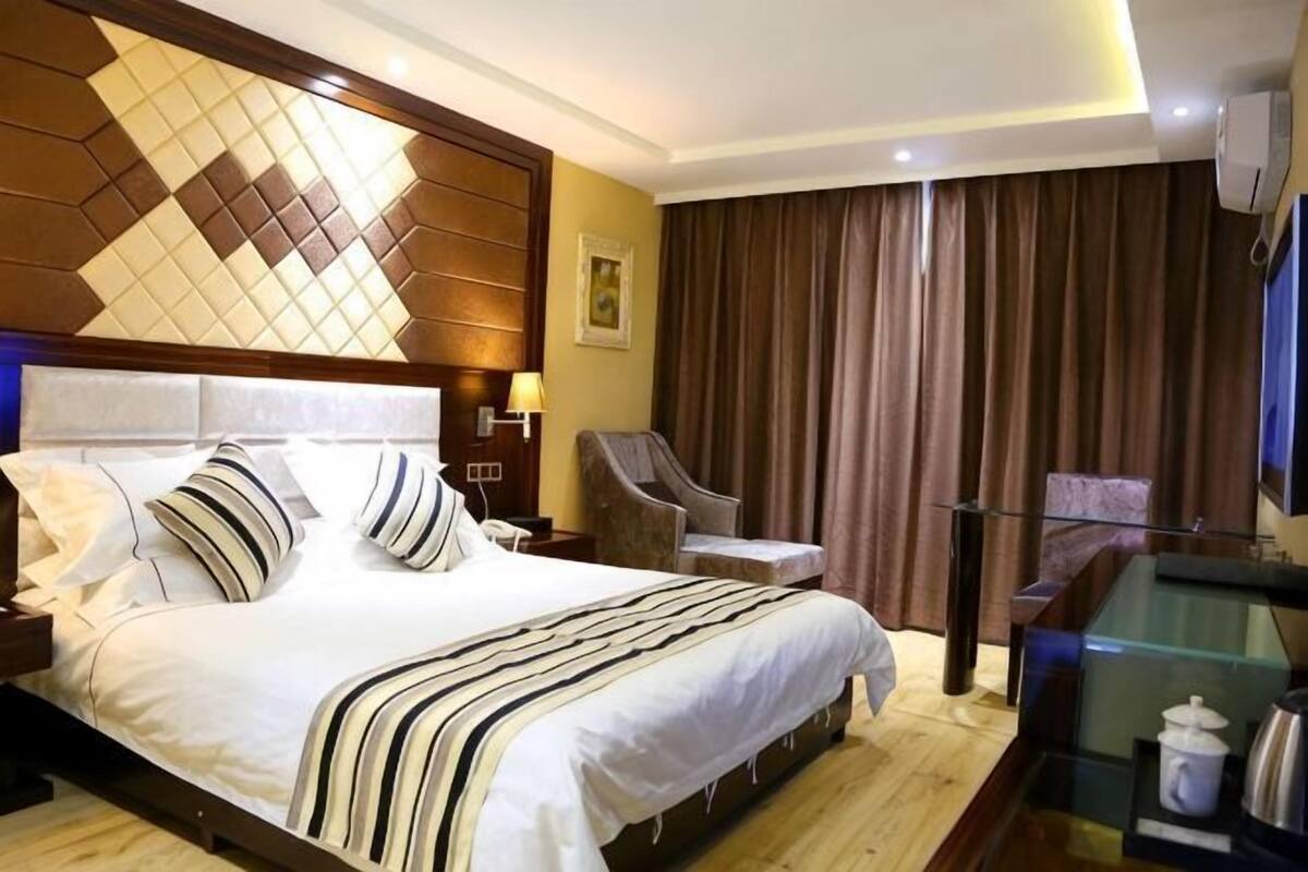 Habitació d'hotel amb un llit gran, una cadira, un escriptori amb taula de vidre i una finestra coberta per una cortina.
