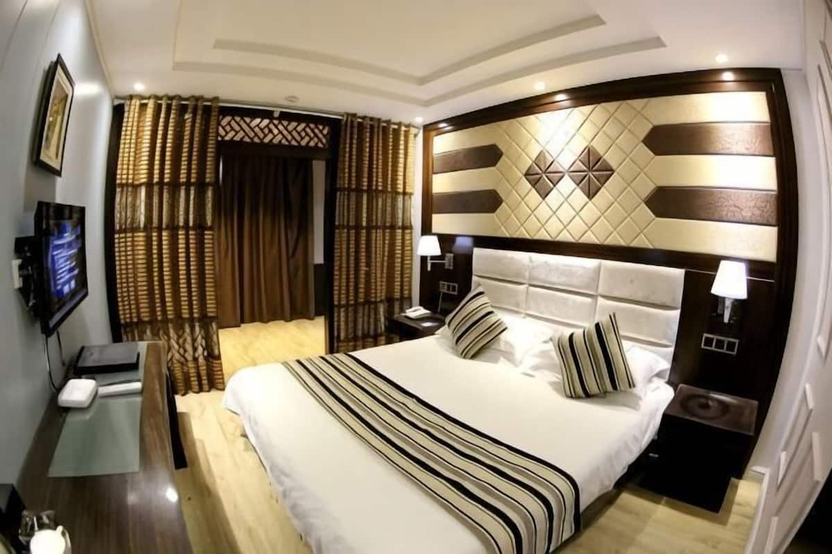 Habitació d'hotel amb un llit gran, un televisor, una taula de treball i una petita taula de nit.