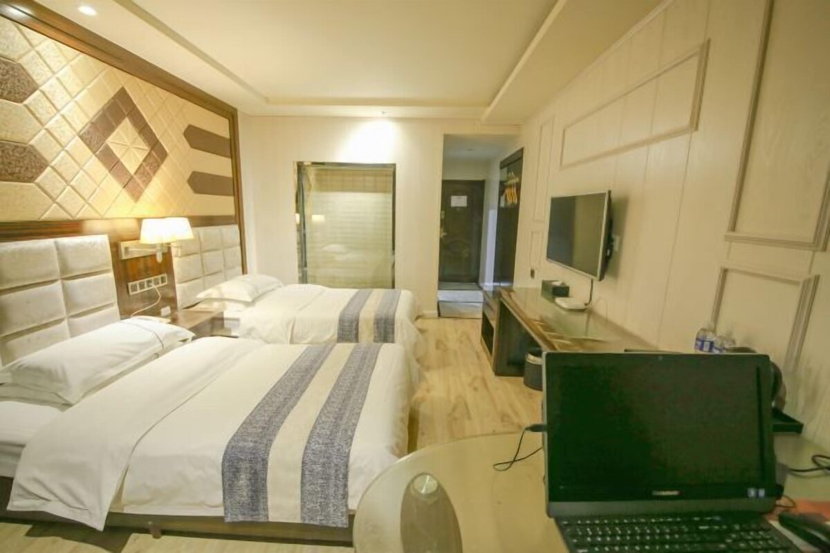 Une chambre d’hôtel avec deux lits, un bureau avec un ordinateur portable, une télévision et un radiateur fixé au mur.