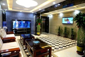 Un vestíbulo de hotel con suelo a cuadros, un televisor de pantalla plana, un sofá, una mesa de centro y plantas en macetas.