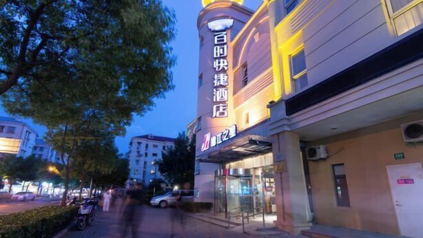 A hotel entrance with a glass facade, a sign with Chinese characters, and a paved walkway.