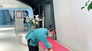 A person cleaning a pink surface in a modern indoor setting with a glass door and a vase of flowers in the background.