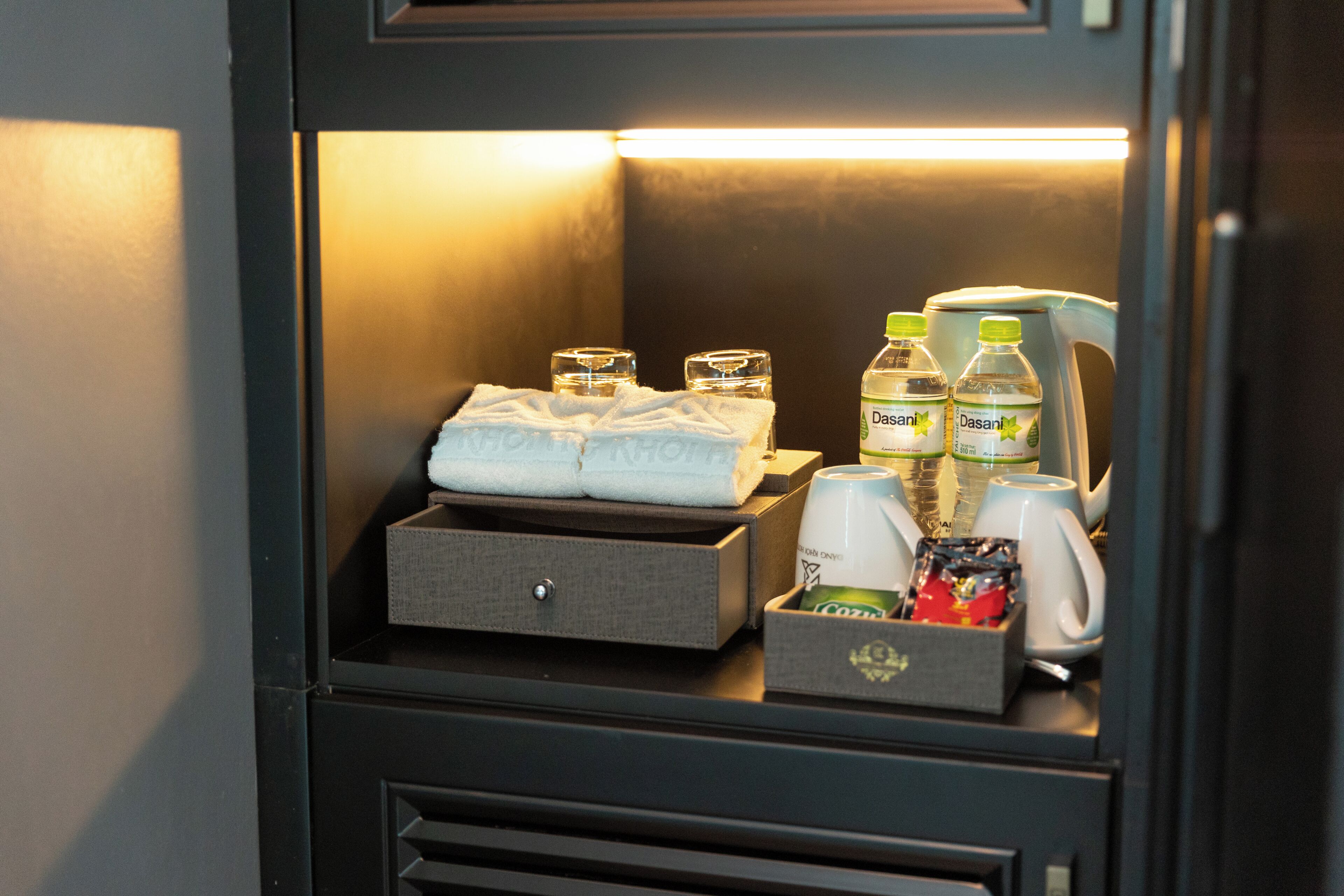Un mini-bar contenant des bouteilles d’eau, une bouteille d’eau Dasani, une boîte de mouchoirs et un petit récipient rempli d’en-cas.