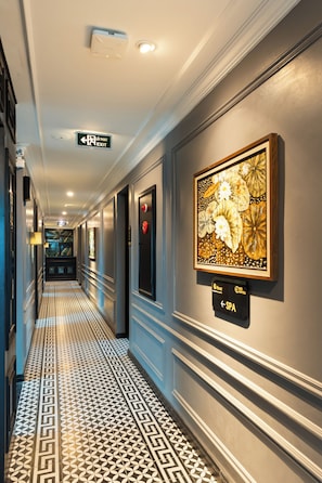 A hotel corridor with patterned flooring, framed artwork, and an exit sign. - YO Hotel (Hai Phong)