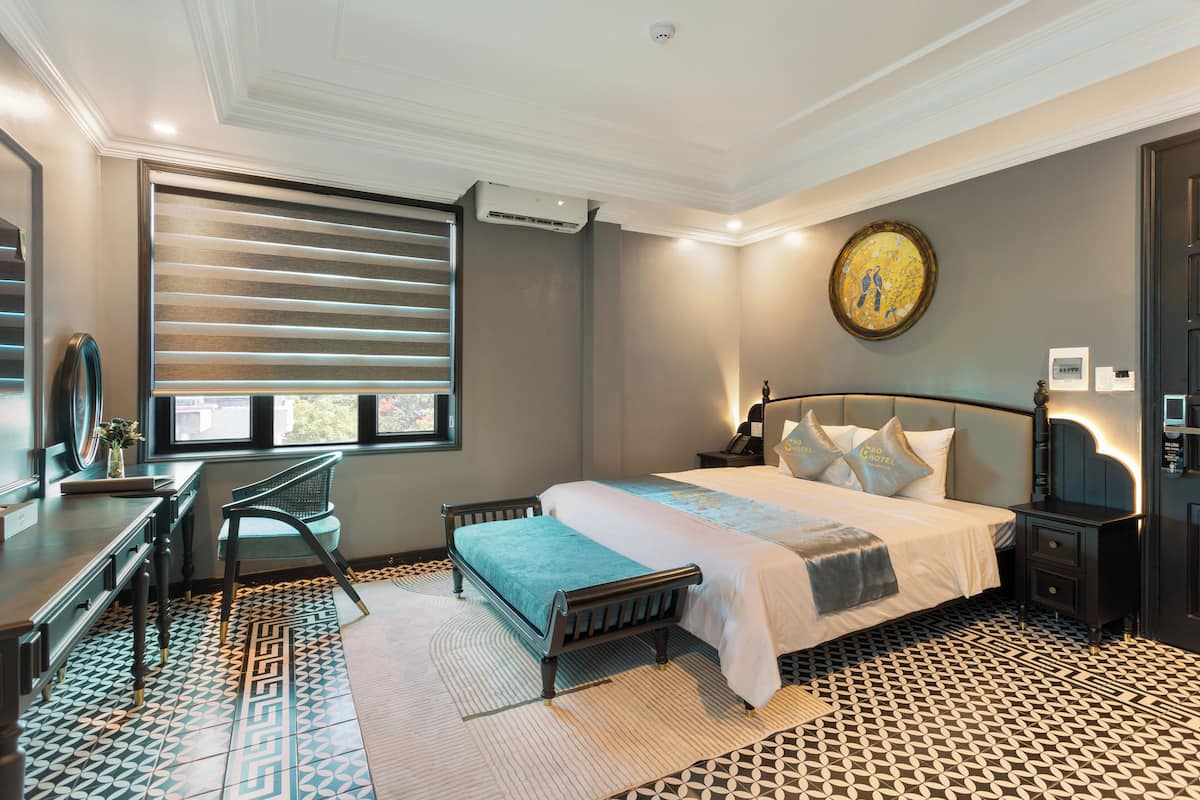 Habitación de hotel con cama, escritorio, silla y un ventanal grande con persianas.