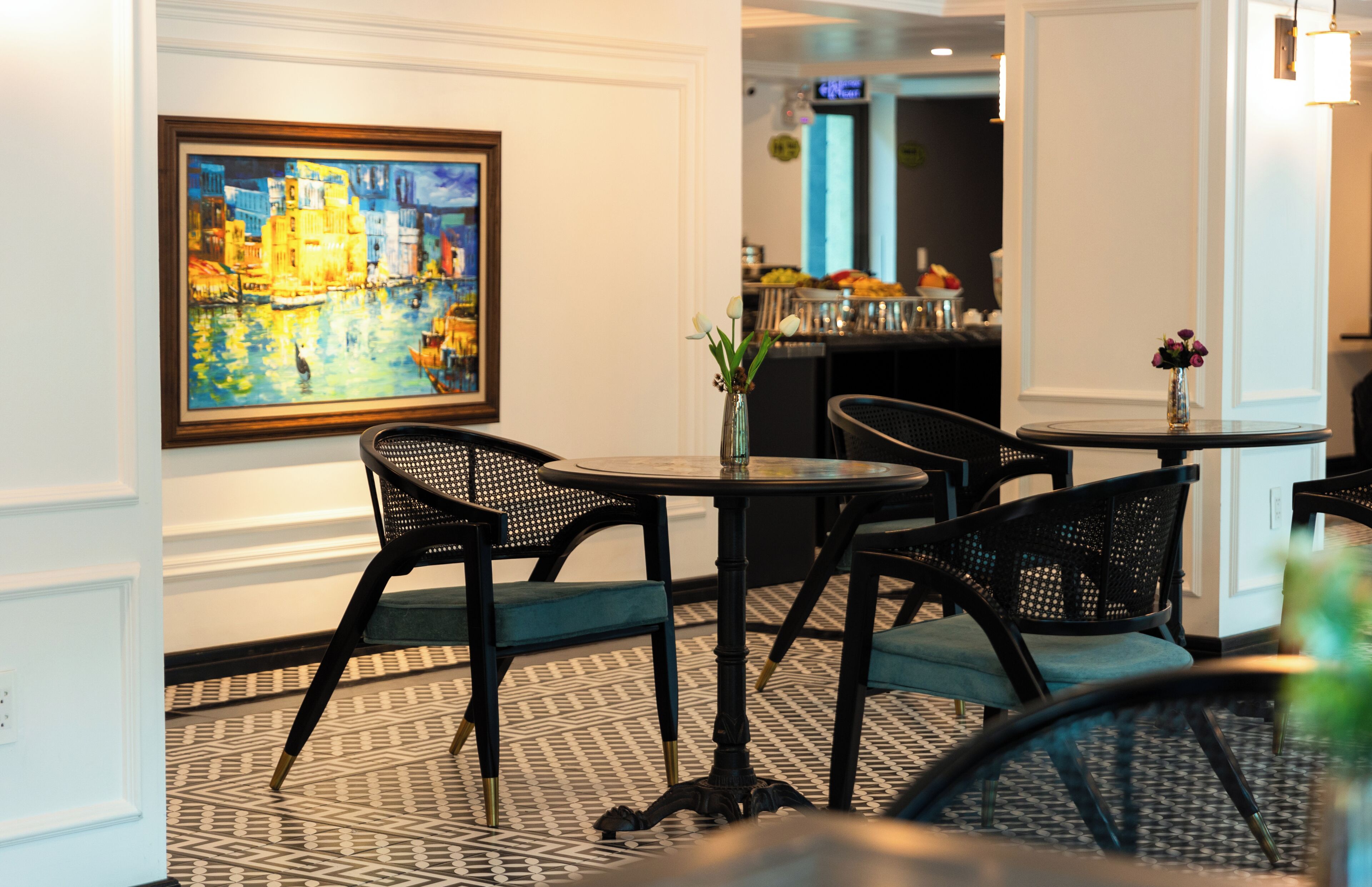 A hotel lobby with a painting, a round table with chairs, and a bar area in the background.