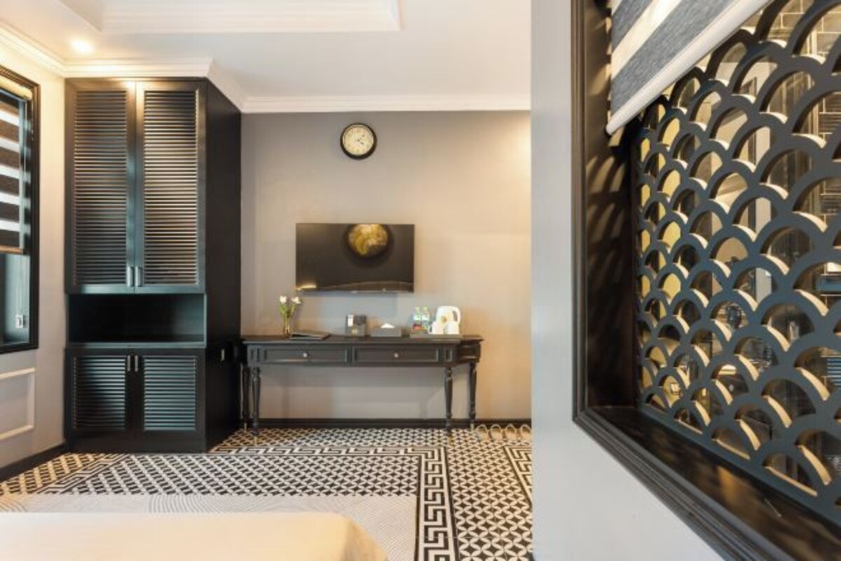 A hotel room with a bed, a desk, a clock, and a decorative screen.
