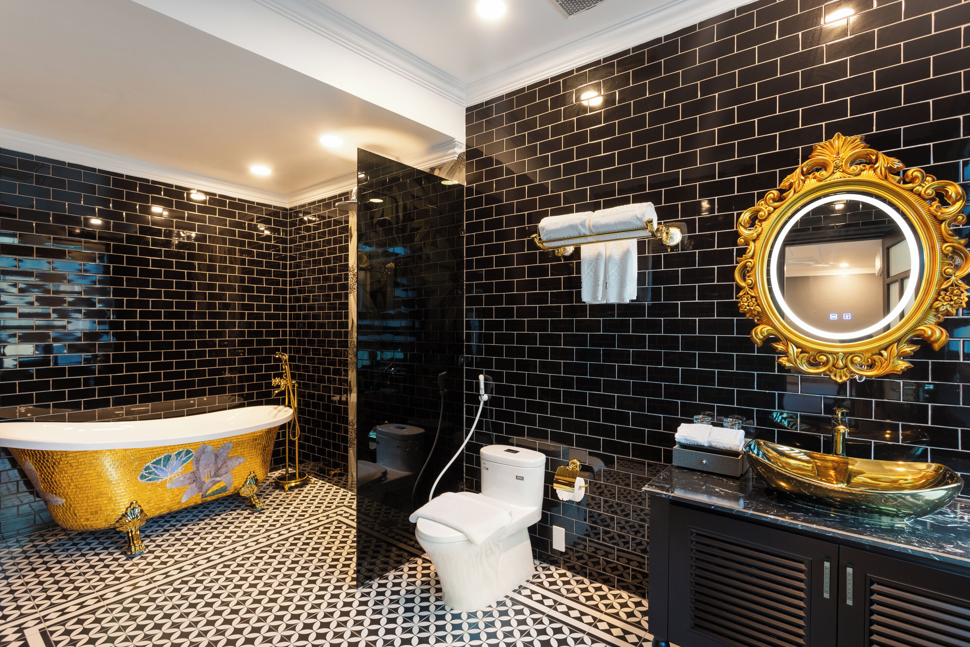 Un baño con una bañera independiente, un inodoro, un lavamanos de estilo dorado y un espejo con un marco decorativo.