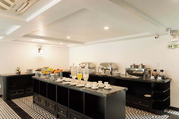A modern kitchen with a central island, equipped with coffee machines, a fruit bowl, and a variety of breakfast items. - YO Hotel (Hai Phong)