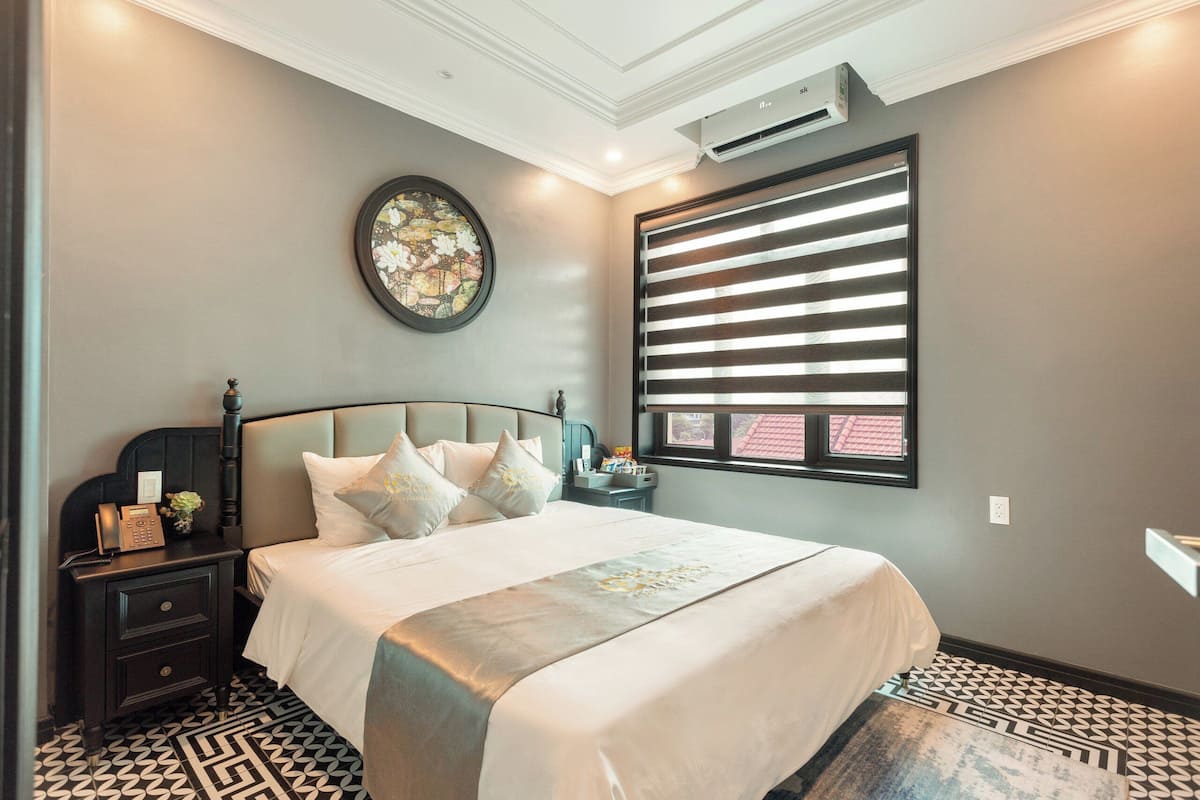 Un dormitorio con cama, mesita de noche, aire acondicionado de pared y una ventana con persianas.
