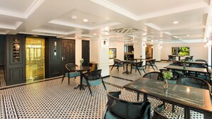 A hotel lobby with a patterned floor, multiple tables and chairs, a bar area, and a decorative wall. - YO Hotel (Hai Phong)