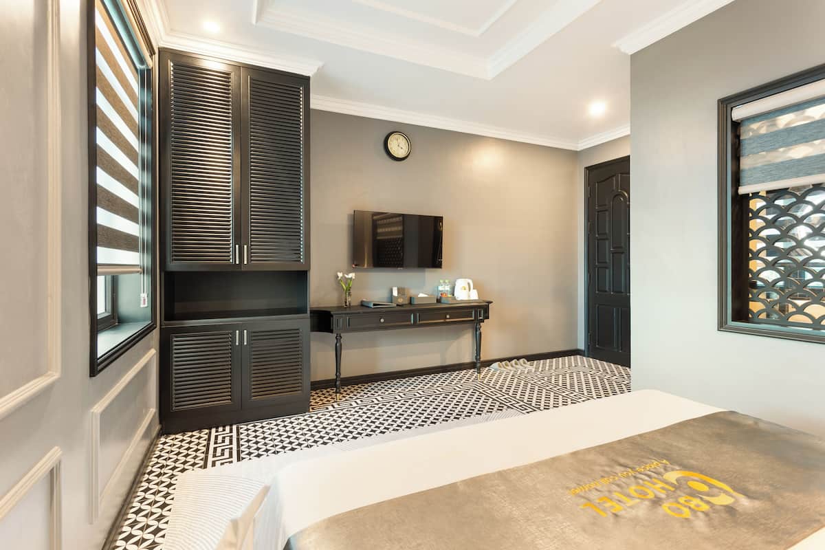 Una habitación de hotel con una cama, un escritorio, un televisor y un reloj en la pared.