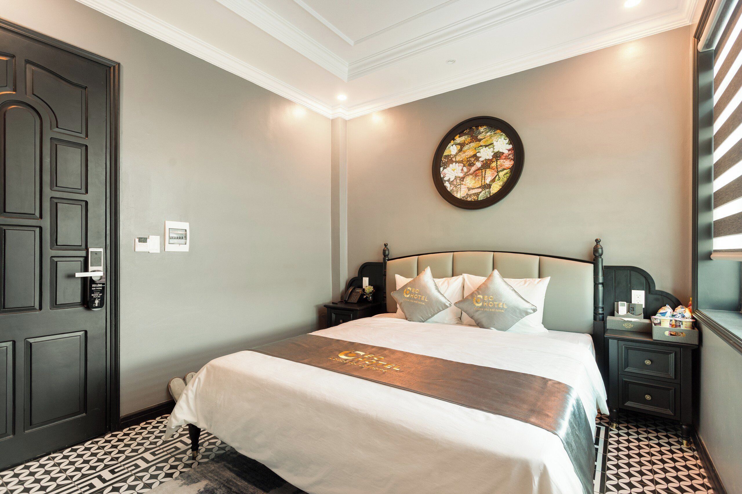 A hotel room with a bed, a nightstand, a wall clock, and a door.