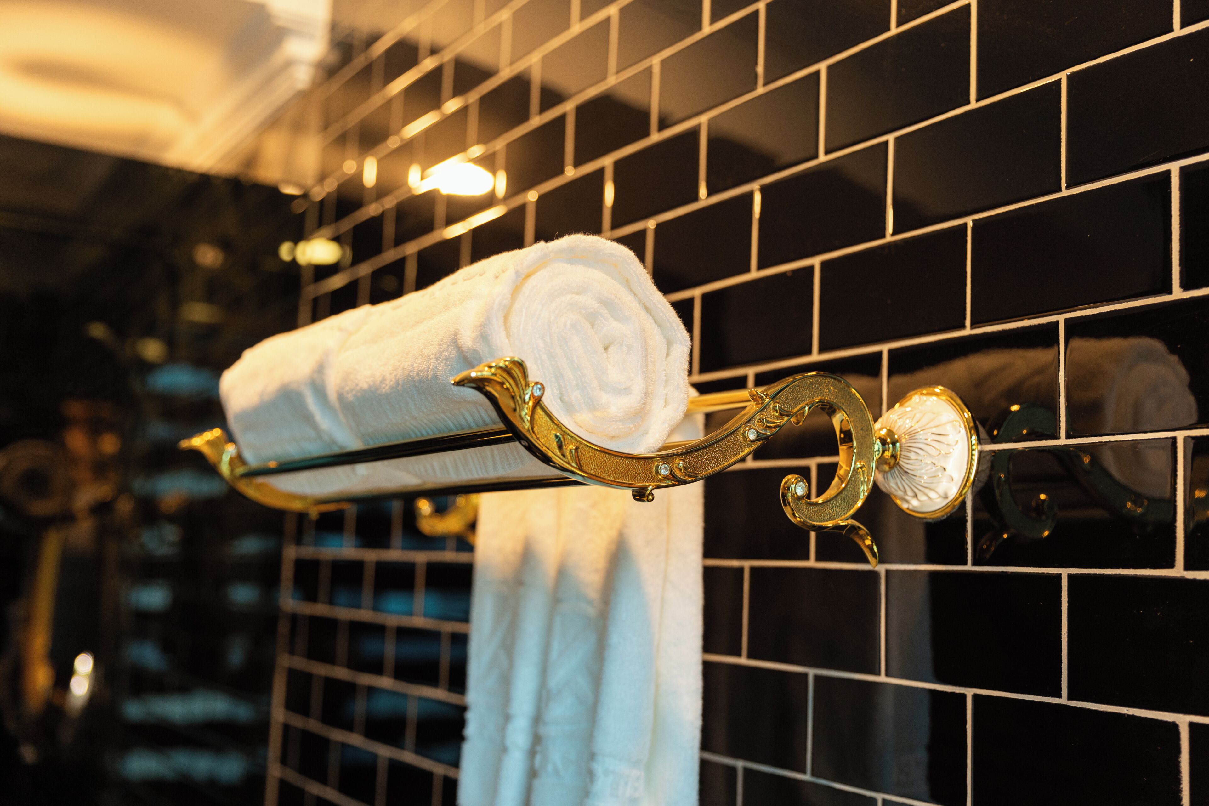 A bathroom with a towel rack holding a rolled towel, a mirror, and a tiled wall.