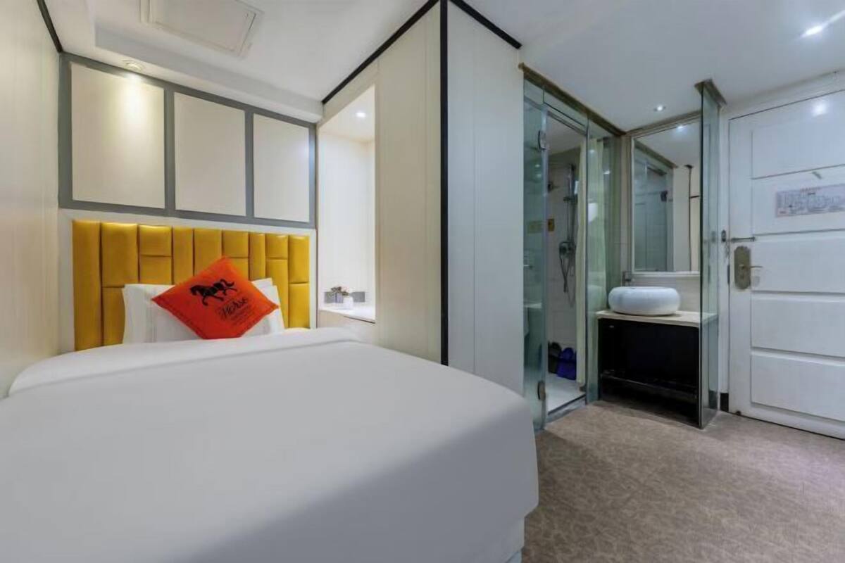 A hotel room with a bed, a glass shower enclosure, and a white wardrobe.