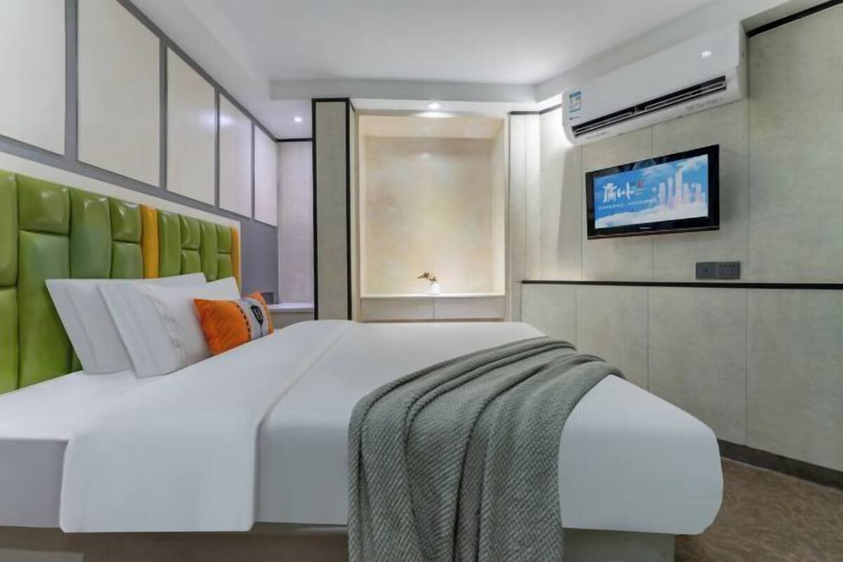 A modern hotel room with a large bed, a television mounted on the wall, and a built-in shelf.