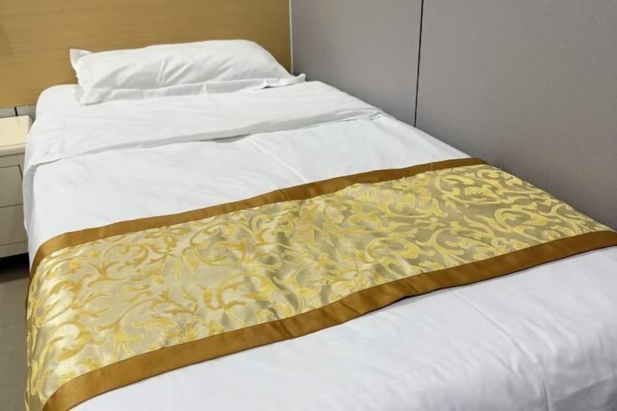 A single bed with white bedding and a gold embroidered bedspread.