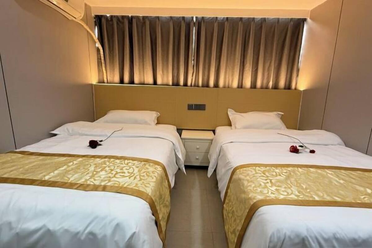 A hotel room with two beds, a headboard, a nightstand, and a curtain.
