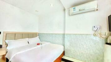 Quarto de hotel com cama, mesa de cabeceira, ar-condicionado fixado na parede e banheiro com porta-toalhas.