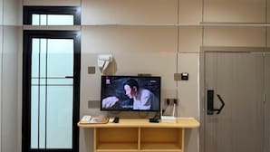 Une chambre d’hôtel moderne avec un téléviseur posé sur un meuble en bois, une porte dotée d’une poignée noire et un interrupteur sur le mur.