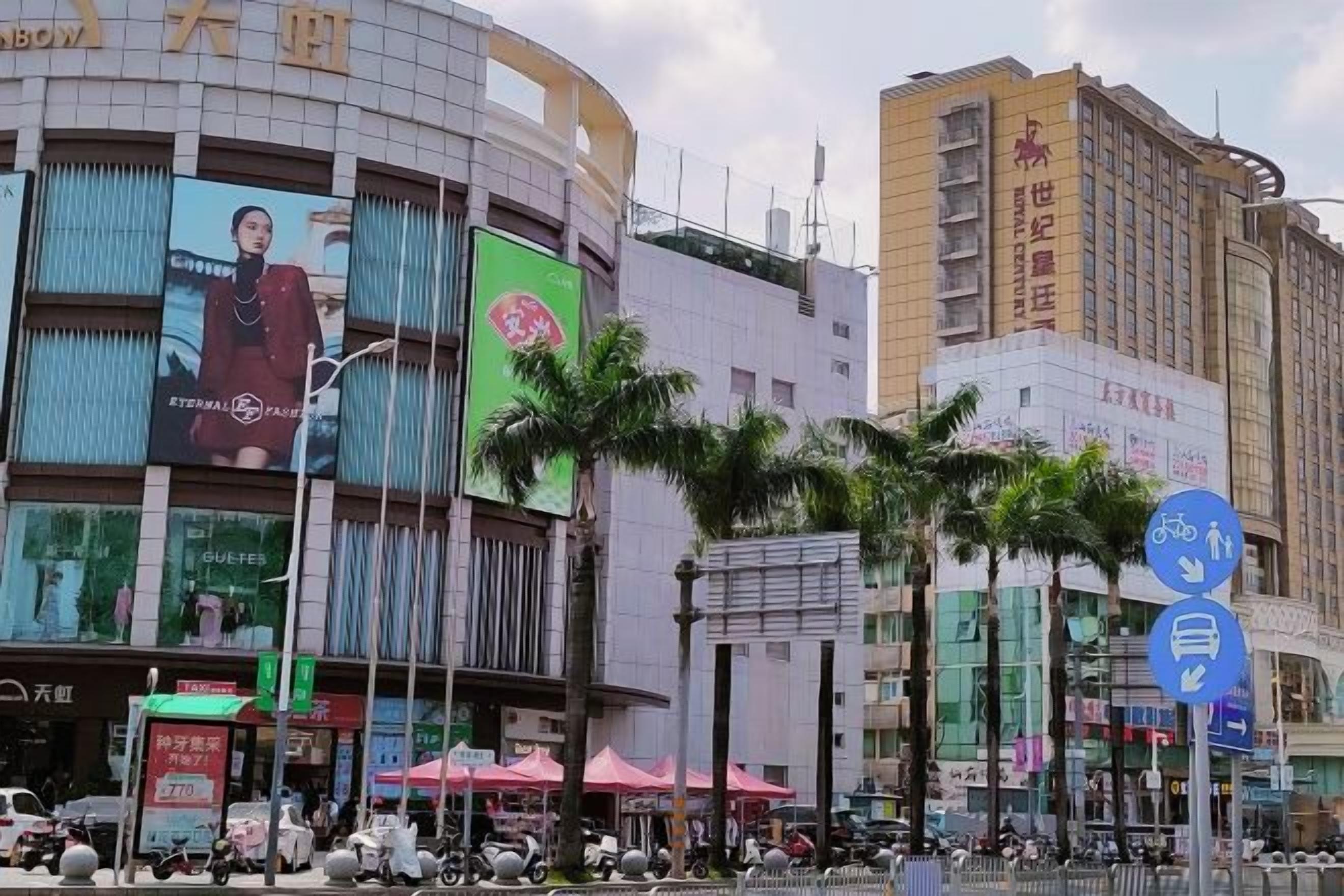 Zona comercial con un edificio curvo que presenta grandes anuncios, palmeras y un paso de peatones.