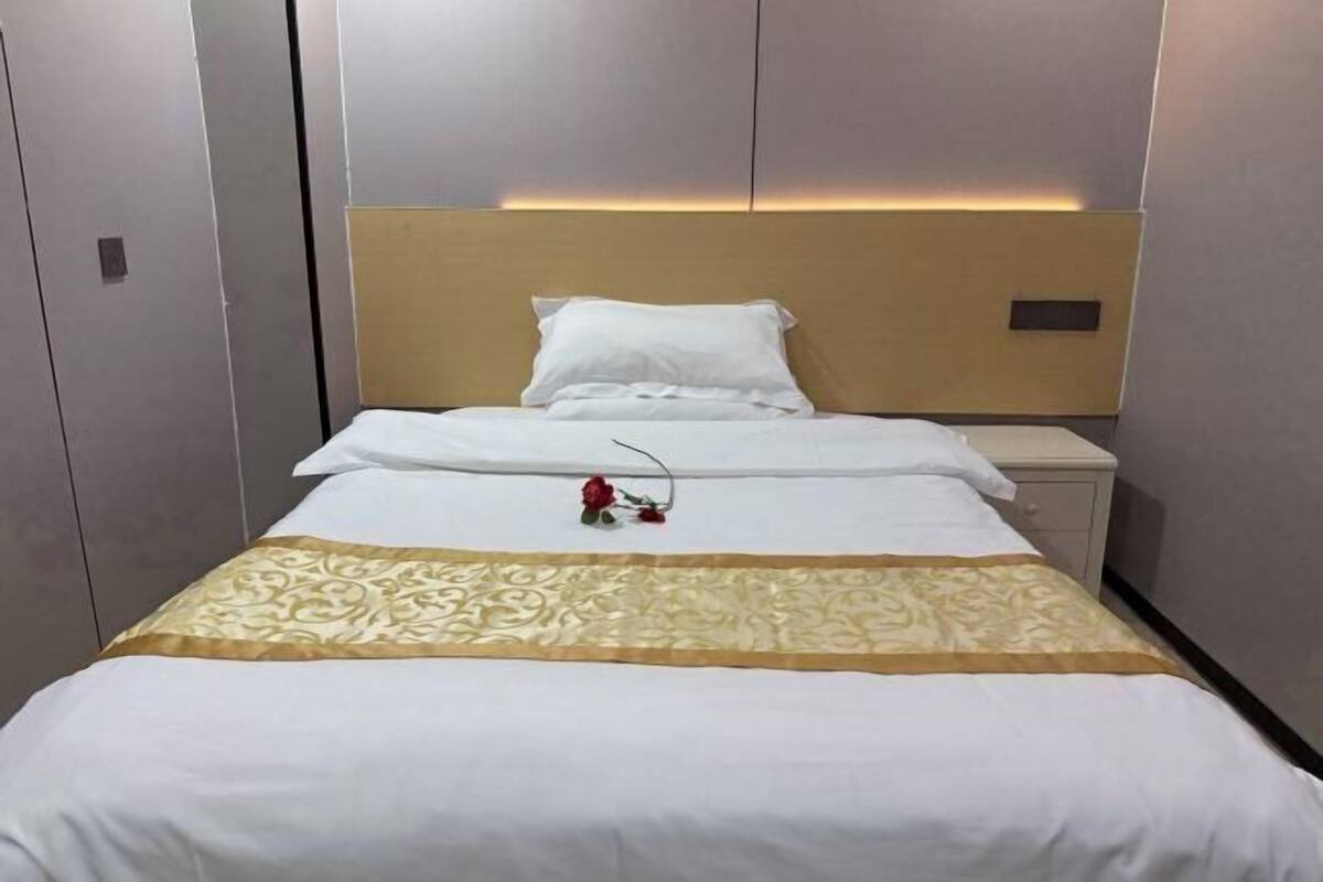 A hotel room with a bed, a nightstand, and a wall-mounted light.
