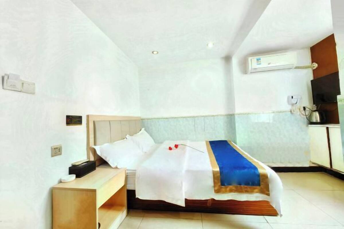 A hotel room with a bed, bedside table, and a small wooden bench.