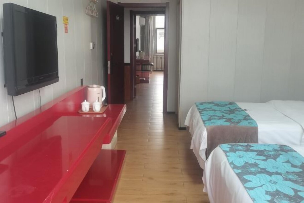 Een hotelkamer met een televisie, een rode bank, twee bedden met bloemenprint en een houten vloer.