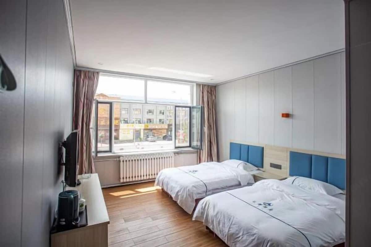 Une chambre d’hôtel avec deux lits, une fenêtre avec des rideaux, un téléviseur à écran plat et une machine à café posée sur une table en bois.