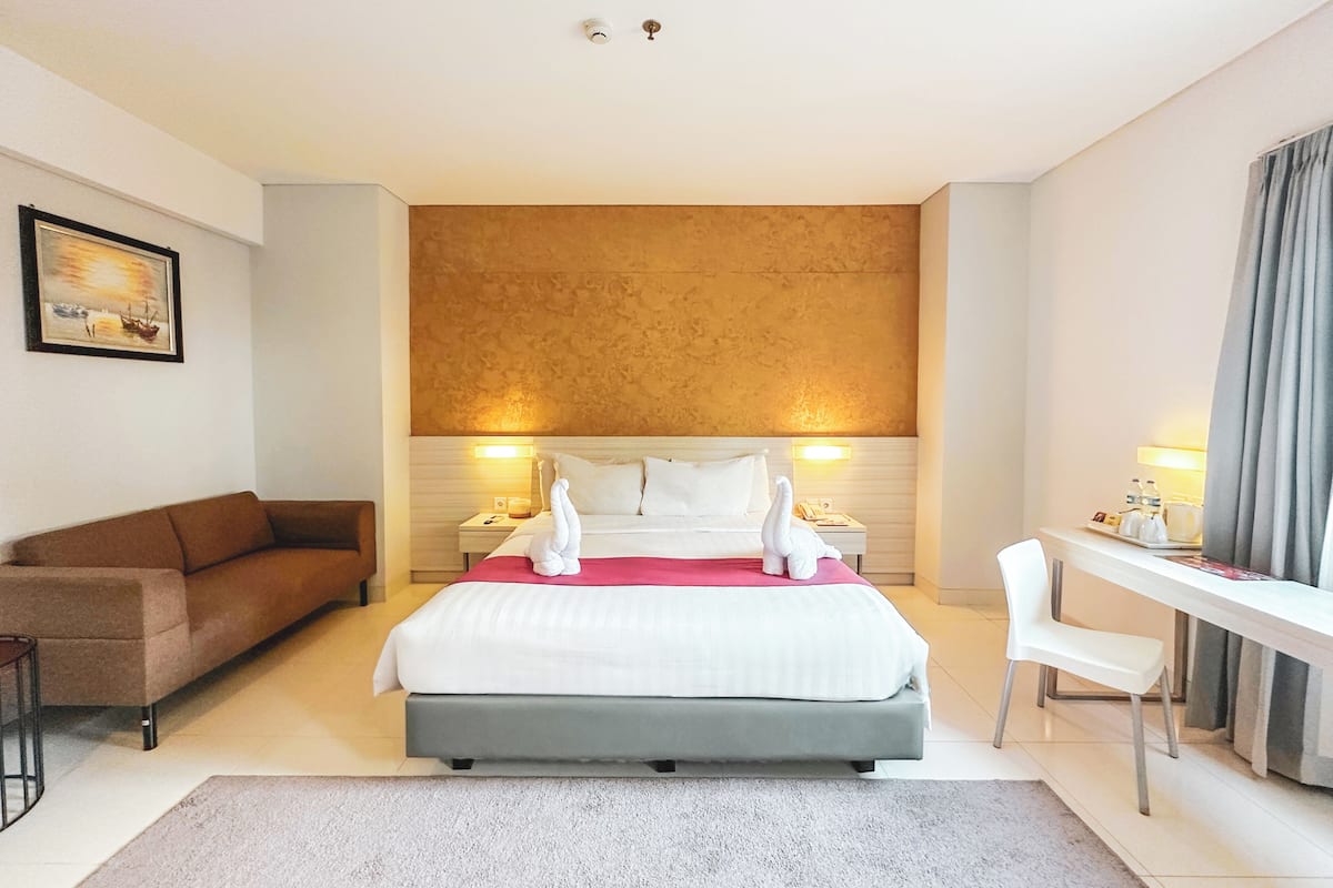 A hotel room with a bed, a desk, a chair, a sofa, and a painting on the wall.