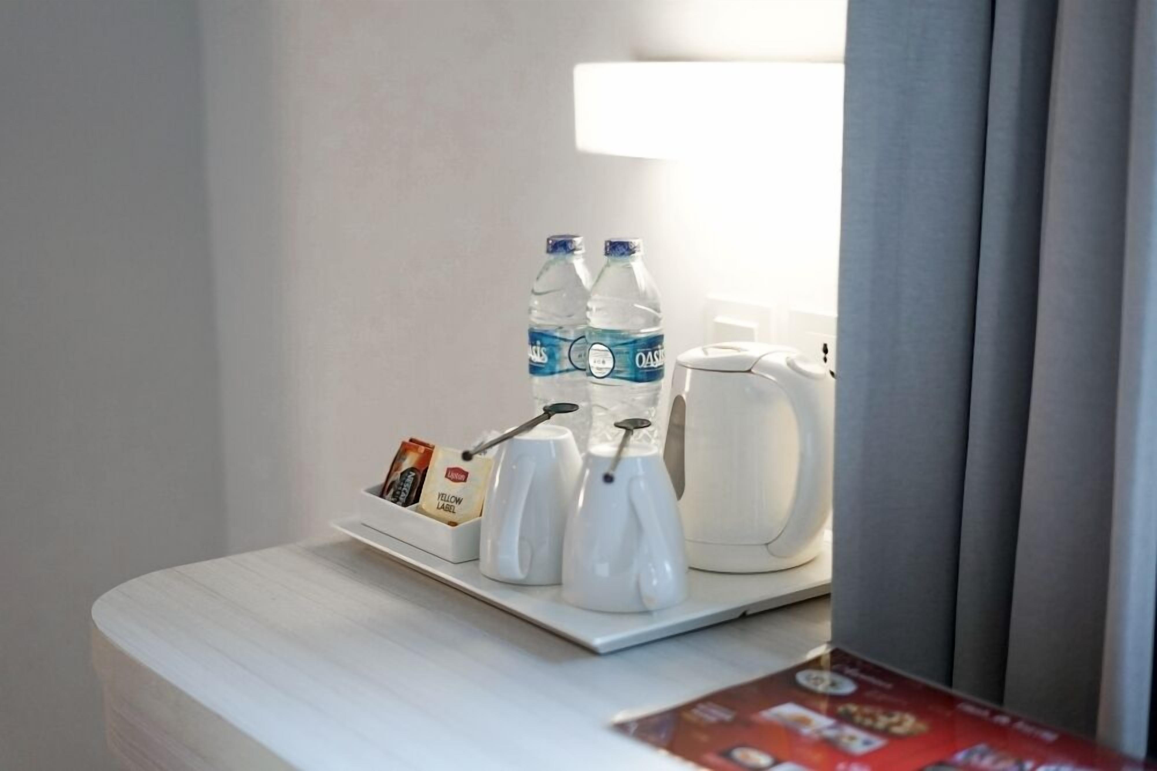 Habitación de hotel con mesita de noche que presenta una botella de agua, una cafetera y una bandeja con una tarjeta y un pequeño recipiente.